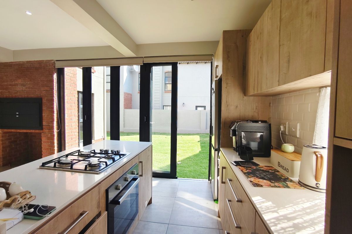 Modern kitchen featuring timber-look cabinetry, stone countertops, gas hob, built-in oven, and seamless access to the rear garden through bi-fold doors.