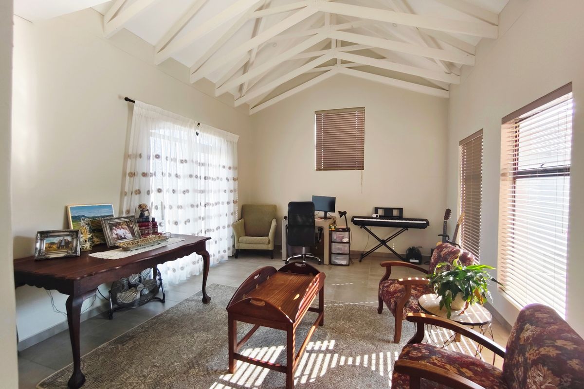 Spacious living area featuring a high vaulted ceiling with exposed timber trusses, tiled flooring, and abundant natural light through large windows and sliding doors.
