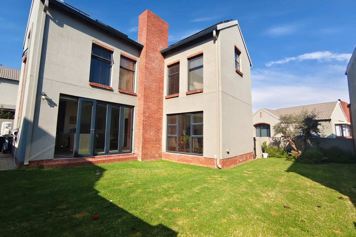 Rear view of a modern double-storey townhouse featuring a prominent brick chimney, large aluminium stacker doors, and a well-maintained private garden.