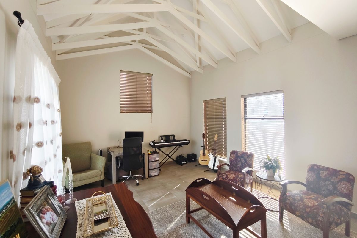 Spacious living area featuring high vaulted ceilings with exposed timber trusses, tiled flooring, and multiple windows fitted with venetian blinds.