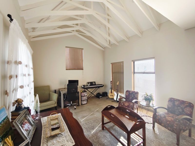 Spacious living area featuring high vaulted ceilings with exposed timber trusses, tiled flooring, and multiple windows fitted with venetian blinds.