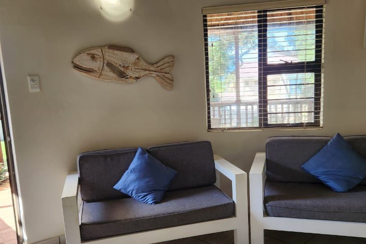 A bright living area featuring tiled floors, aluminium window frames with venetian blinds, and direct access to an outdoor patio space.