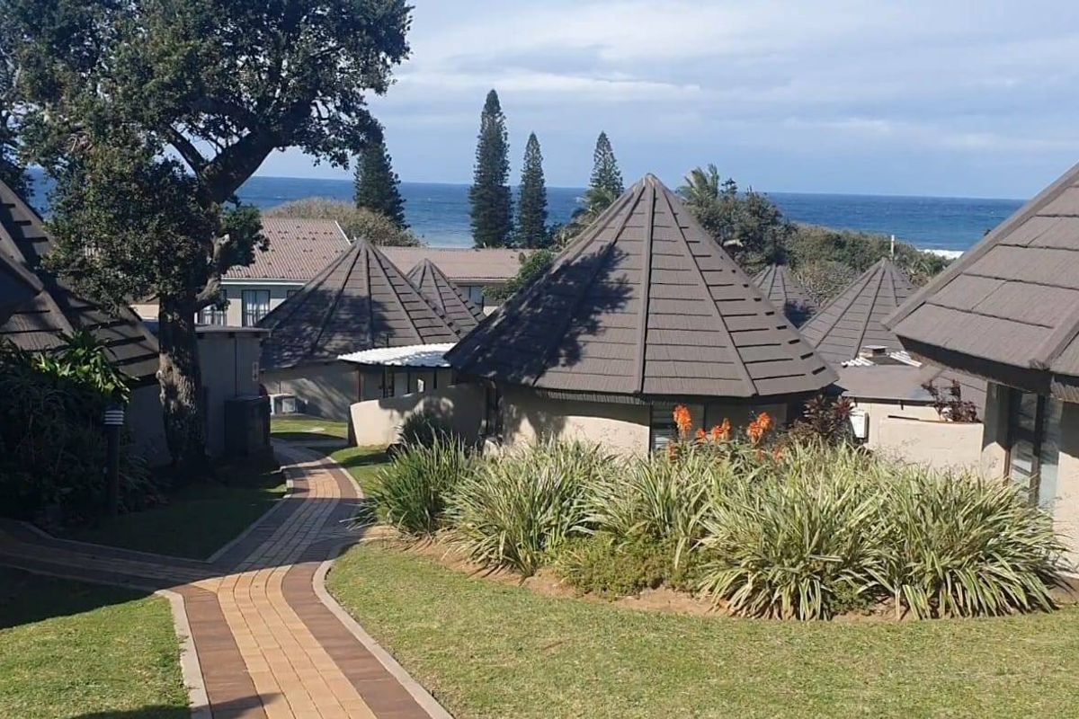 A scenic view of the townhouse complex exterior featuring paved walkways, landscaped gardens, and distinctive tiled roofs with a coastal backdrop.
