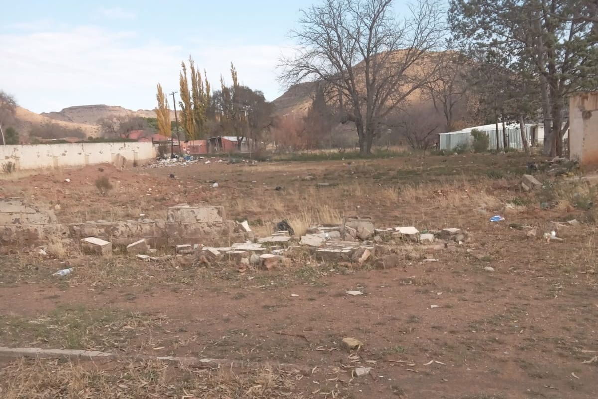 A vacant residential plot featuring a boundary wall, mountain views, and scattered debris, offering a blank canvas for future development.