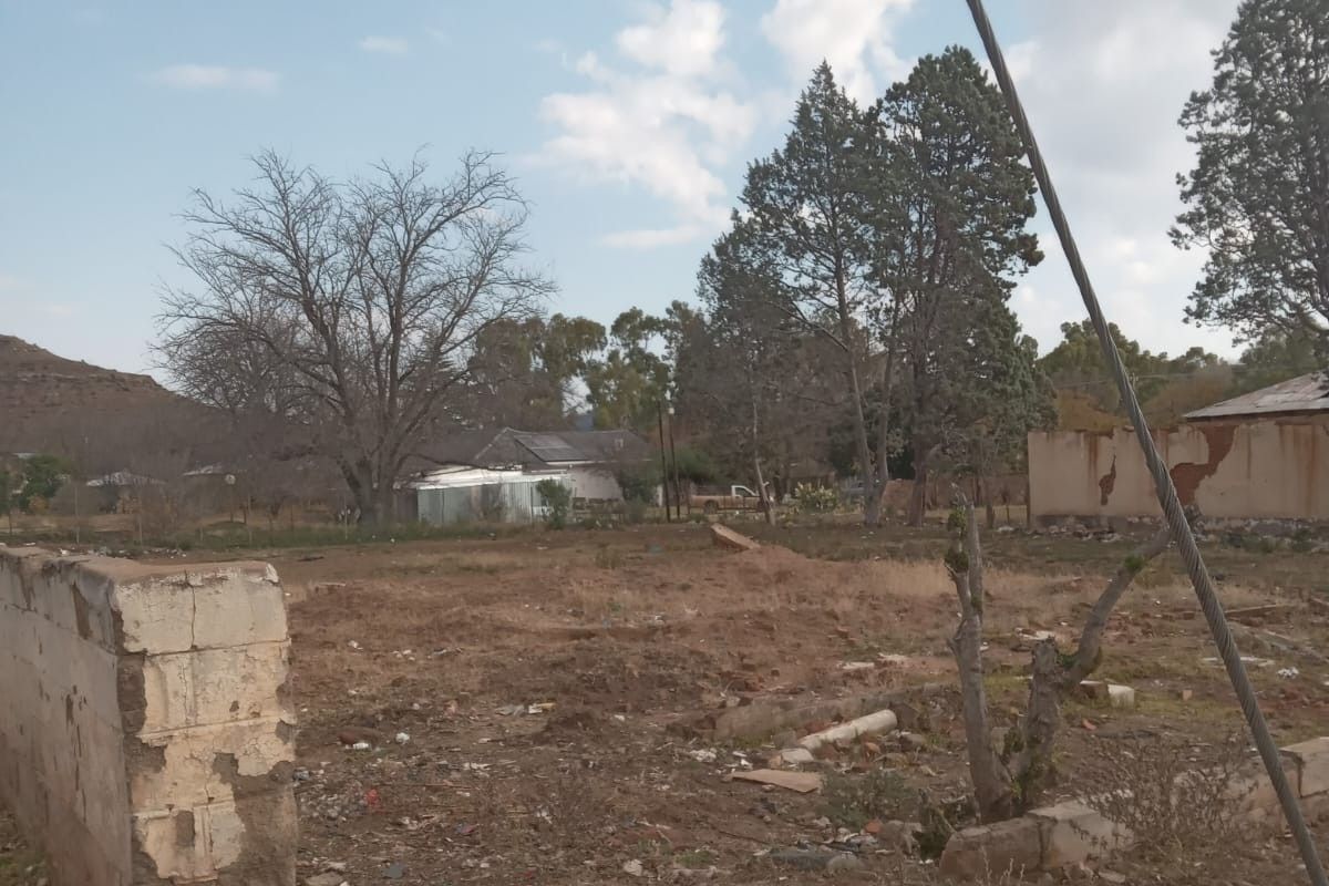 A view of a vacant residential plot featuring a weathered boundary wall and open land, suitable for new development.