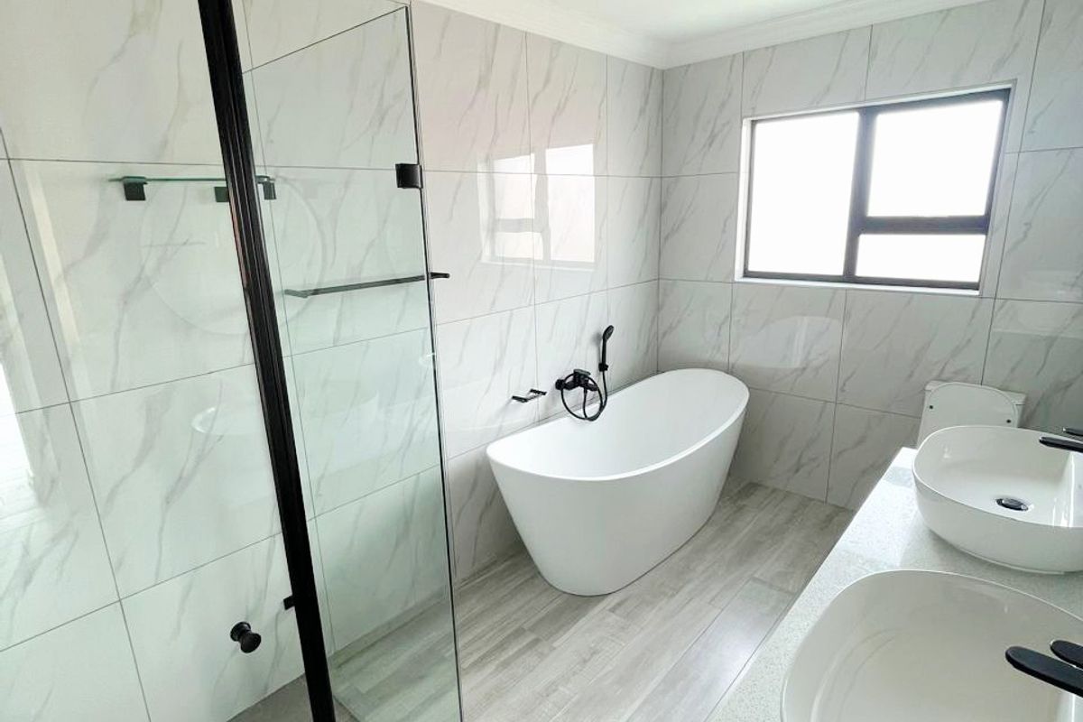 Modern bathroom featuring a freestanding bathtub, walk-in shower with black frame, and a double vanity with contemporary black fixtures and marble-look tiling.