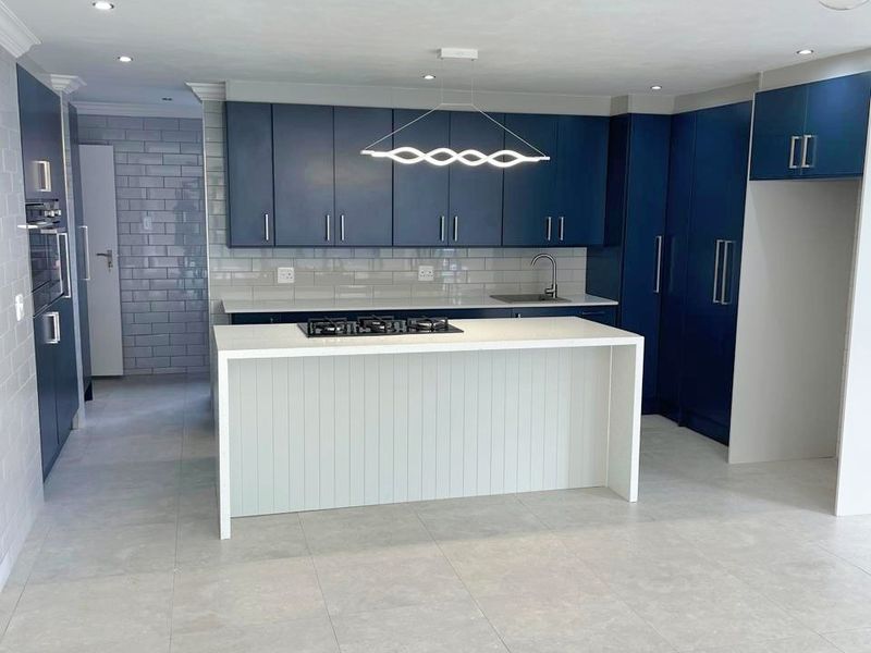Modern kitchen featuring dark blue cabinetry, a central island with a gas hob, stone countertops, and a stylish subway tile backsplash.
