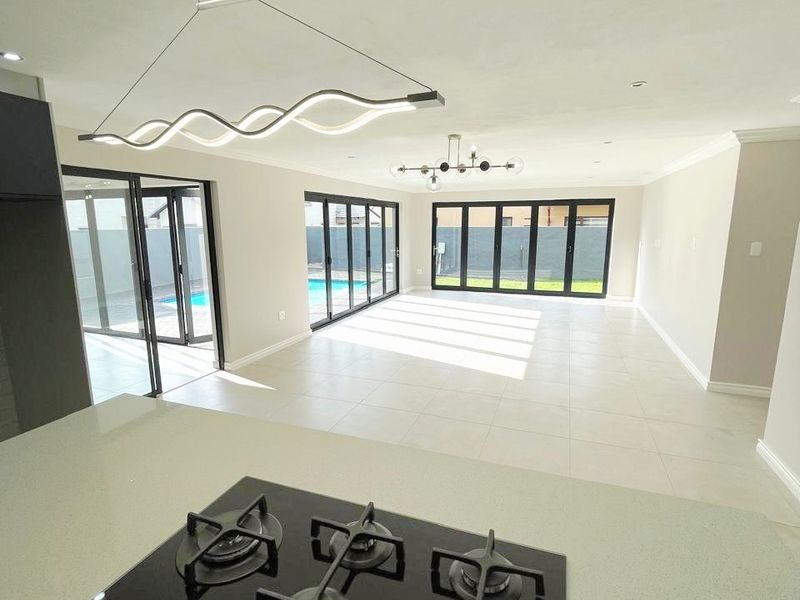 Spacious open-plan living area featuring a modern kitchen with gas cooktop, stone island, and large stacking doors opening to the pool area.