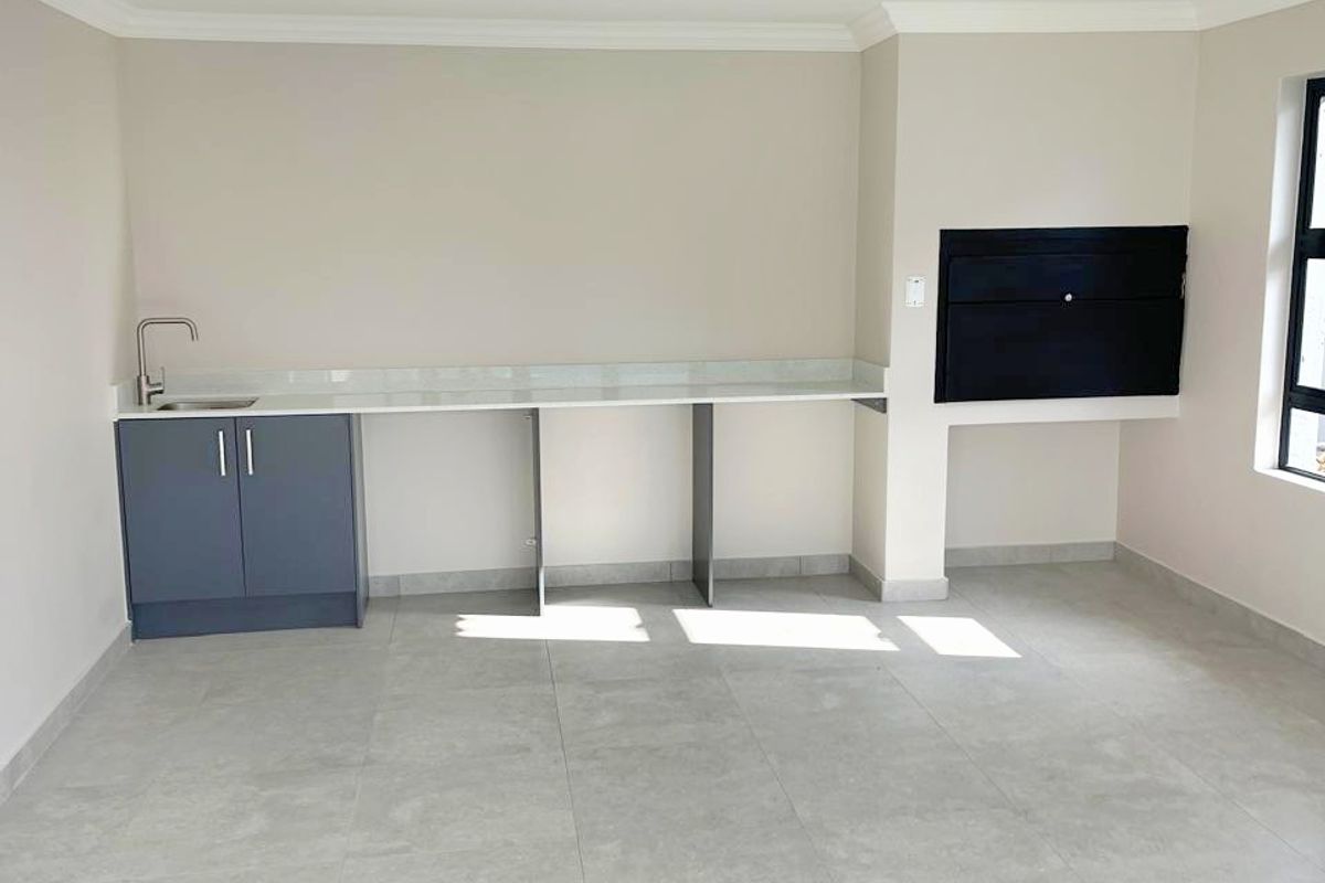 A bright, modern living area featuring large format floor tiles, a built-in braai, and a sleek kitchenette with stone countertops and a sink.