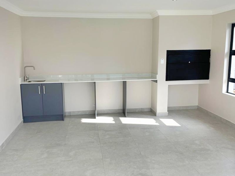 A bright, modern living area featuring large format floor tiles, a built-in braai, and a sleek kitchenette with stone countertops and a sink.