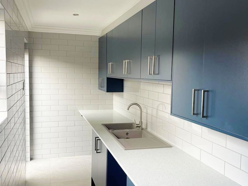 A modern, clean scullery featuring navy blue cabinetry, white quartz countertops, and a subway tile backsplash with an undermount sink.