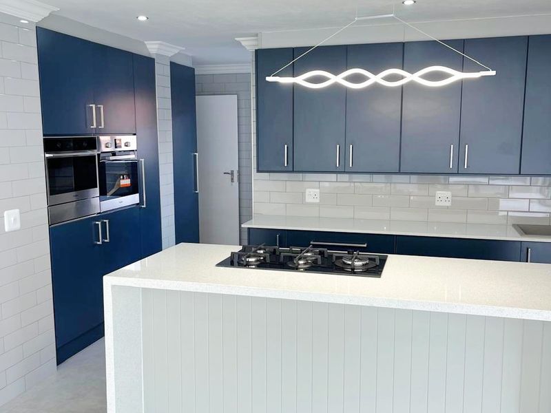 Modern kitchen featuring navy blue cabinetry, a central island with a gas hob, quartz countertops, and contemporary lighting fixtures.