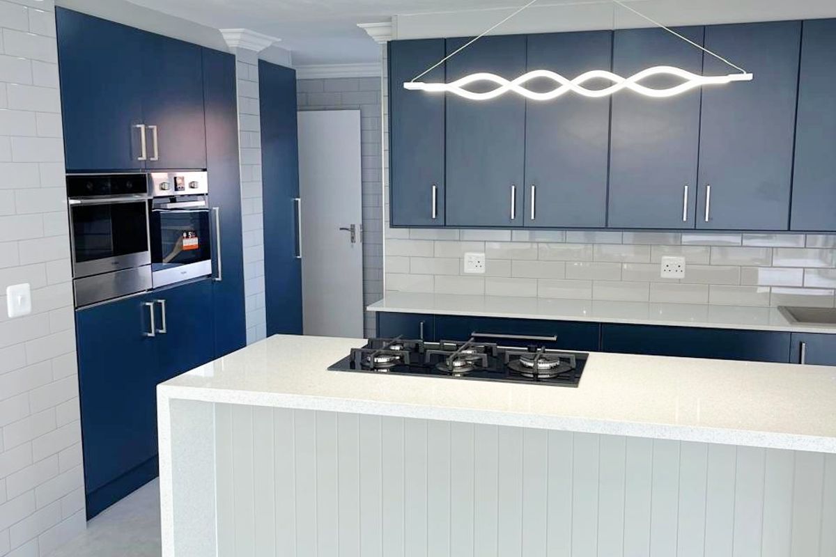 Modern kitchen featuring navy blue cabinetry, a central island with a gas hob, quartz countertops, and contemporary lighting fixtures.