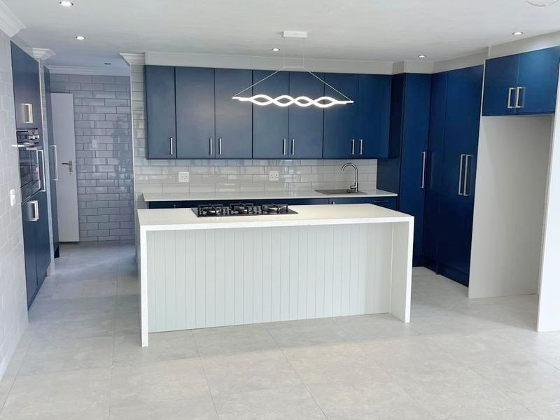 Modern kitchen featuring navy blue cabinetry, a central island with a gas cooktop, subway tile backsplash, and neutral floor tiles.
