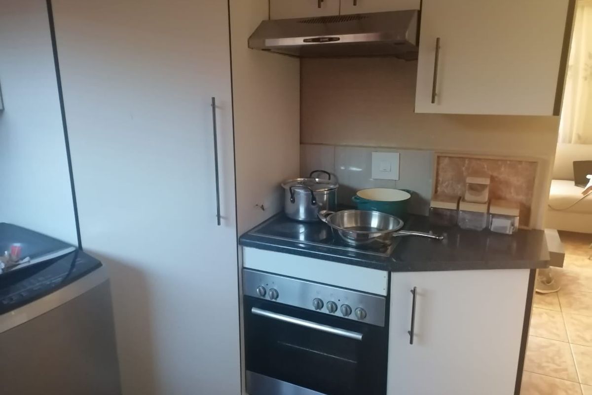 Compact kitchen area featuring built-in cabinetry, a stainless steel oven, electric hob, and extractor fan with tiled splashback.