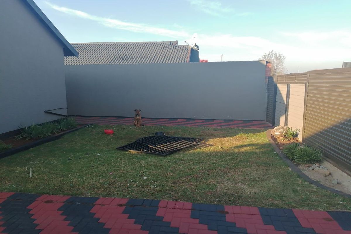 A private rear garden area featuring a paved patio, perimeter boundary walls, and metal fencing, providing a secure outdoor space.