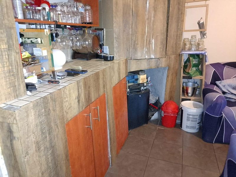 A built-in home bar area featuring tiled countertops, laminate cabinetry, and integrated glassware storage, currently showing signs of wear and dated finishes.