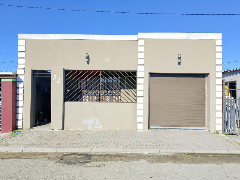 Front elevation of a single-story house featuring a paved driveway, integrated garage, and security-gated entrance.