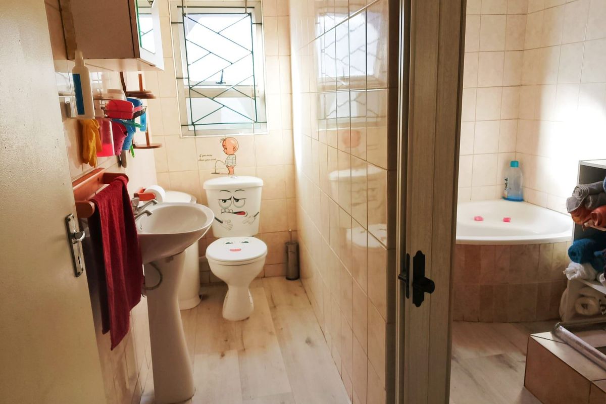 A functional bathroom featuring a pedestal basin, toilet, and a corner bathtub with tiled walls and laminate flooring.