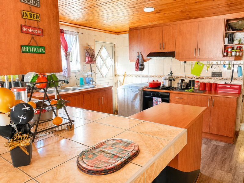 A functional kitchen featuring wooden cabinetry, tiled countertops, a built-in oven with extractor fan, and a timber-paneled ceiling.