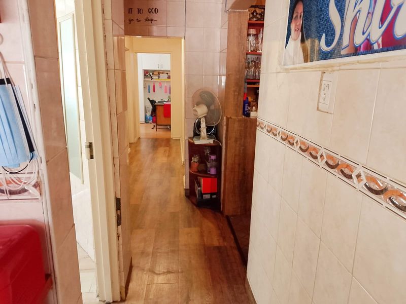 A narrow hallway featuring tiled walls and laminate flooring, providing access to adjacent rooms within the home.