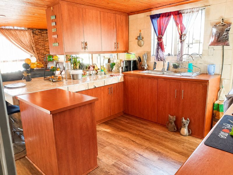 A functional kitchen featuring wooden cabinetry, tiled countertops, a double basin sink, and warm timber ceiling finishes.
