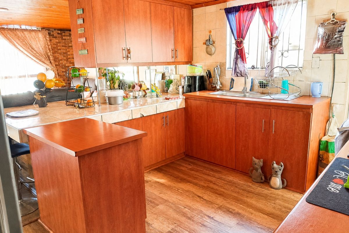 A functional kitchen featuring wooden cabinetry, tiled countertops, a double basin sink, and warm timber ceiling finishes.