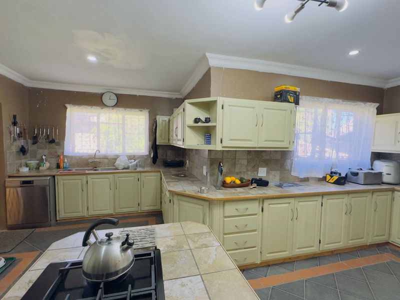 Spacious kitchen featuring extensive built-in cabinetry, tiled countertops, and a central island with a gas hob, offering a functional layout with potential for cosmetic updates.