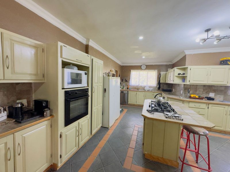 Spacious kitchen featuring a central island with a gas hob, built-in oven, ample cabinetry, and tiled flooring, offering significant potential for modernization.