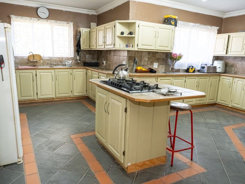 Spacious kitchen featuring a central island with a gas hob, ample built-in cabinetry, tiled backsplash, and durable tiled flooring throughout.