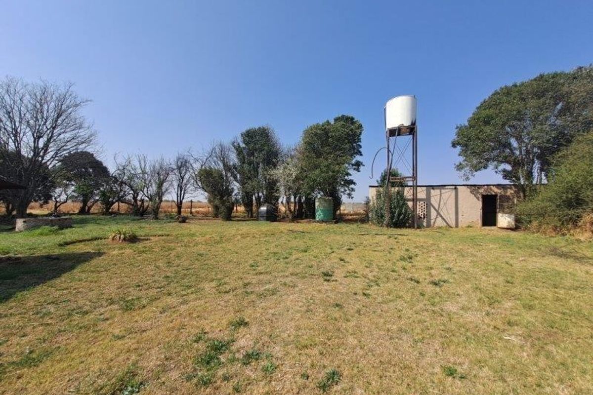 Expansive farm garden area featuring a raised water tank on a steel stand and a small outbuilding structure.