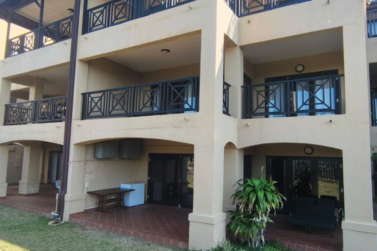 Rear view of the apartment building featuring ground floor tiled patios and upper-level balconies with black metal balustrades and sliding door access.