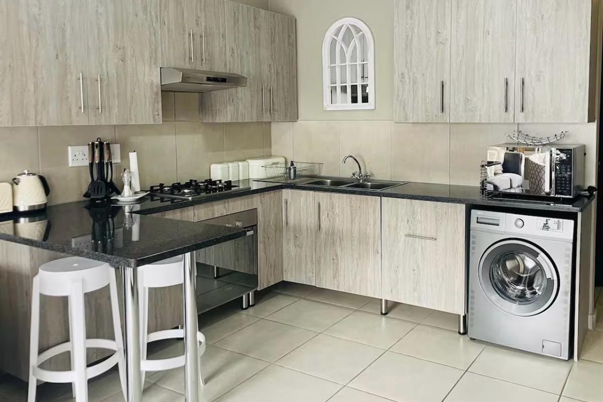 Modern kitchen featuring light wood-grain cabinetry, granite countertops, gas hob, built-in oven, extractor fan, and dedicated space for a washing machine.