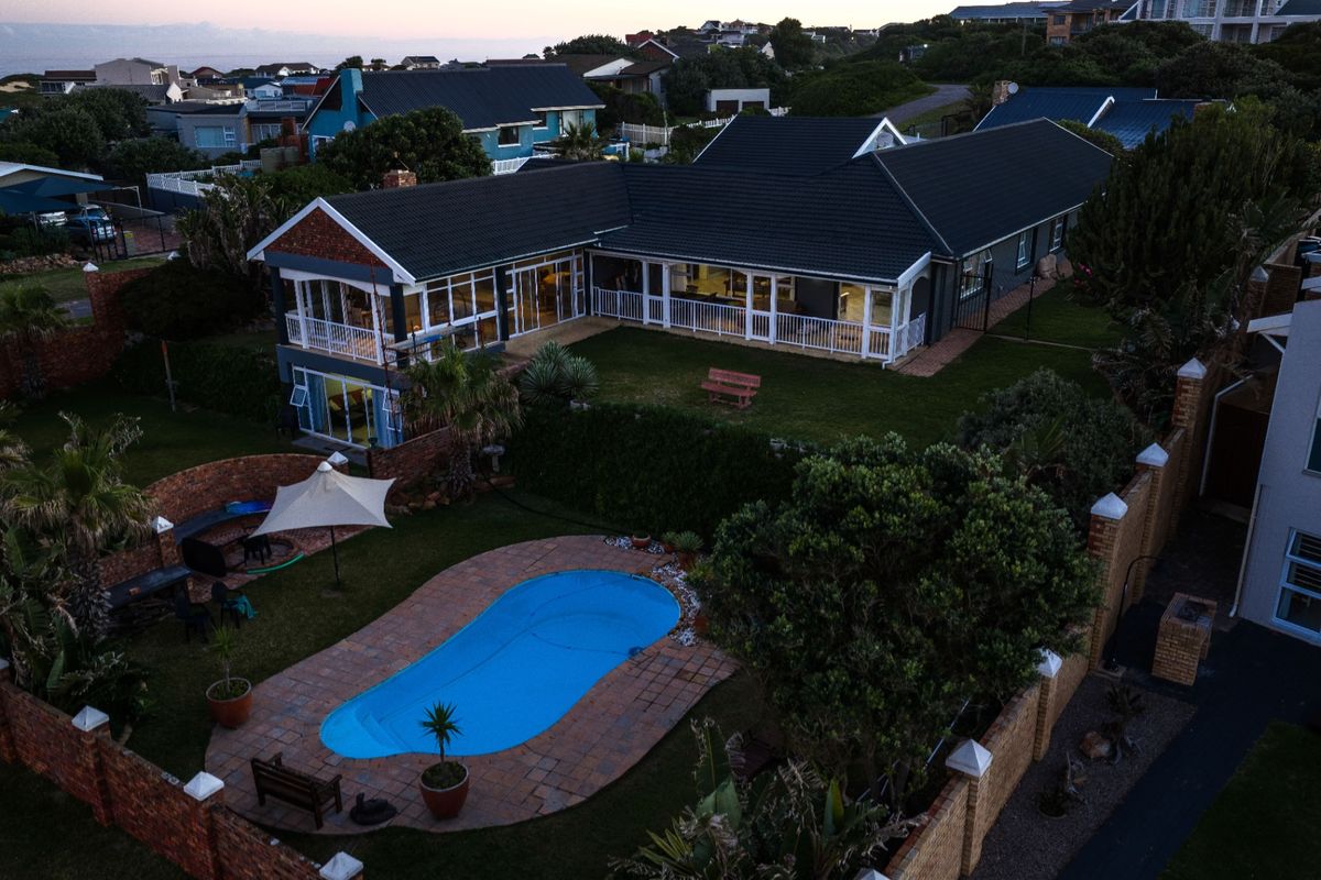 Aerial view of a residential property featuring a swimming pool, landscaped garden, covered patio, and a multi-level house with a tiled roof.