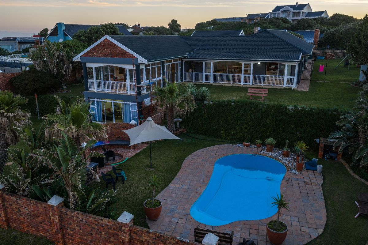 Aerial view of the rear property featuring a swimming pool, paved patio area, covered balcony, and landscaped garden with brick boundary walling.