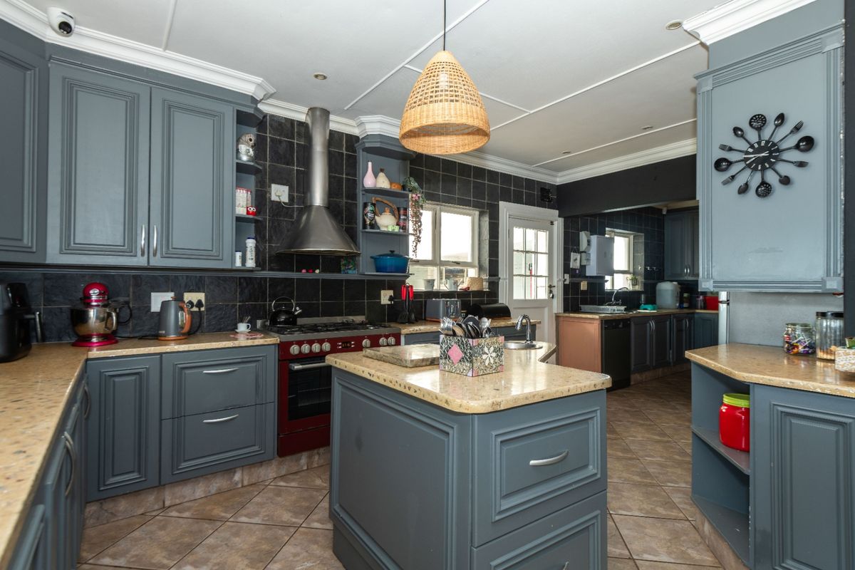 Spacious kitchen featuring dark grey cabinetry, stone countertops, a central island, and a dedicated scullery area with tiled finishes.