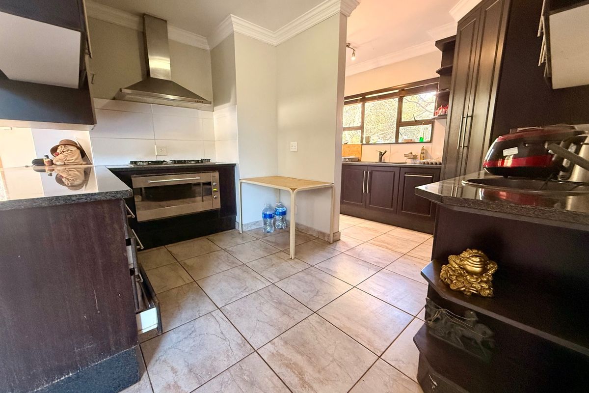 A functional kitchen featuring dark cabinetry, granite countertops, built-in oven, gas hob, and a separate scullery area with a double sink.