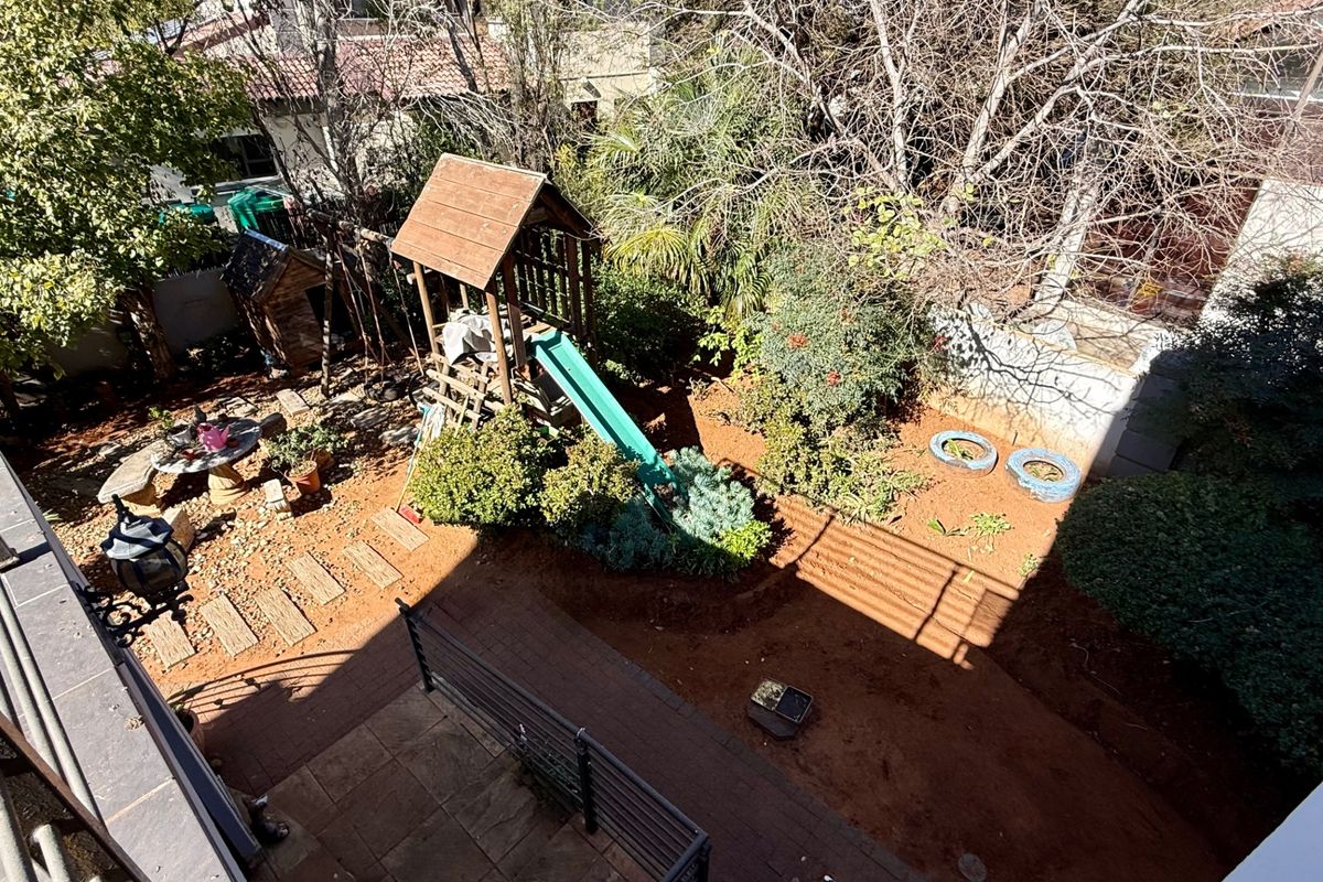 An elevated view of a rear garden featuring a paved patio area, metal railings, and established landscaping.