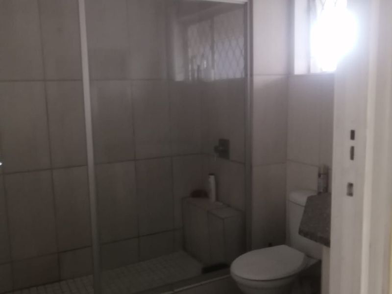 A functional bathroom featuring a glass-enclosed shower, a standard toilet, and tiled finishes throughout, providing a clean and practical space.
