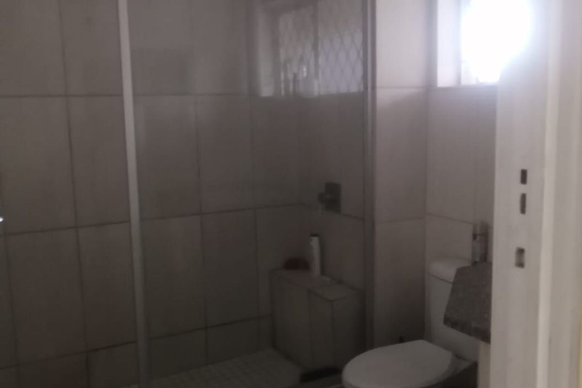 A functional bathroom featuring a glass-enclosed shower, a standard toilet, and tiled finishes throughout, providing a clean and practical space.