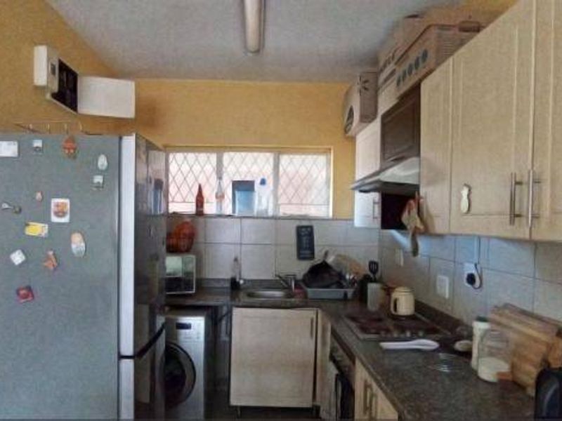 A functional kitchen featuring built-in cabinetry, a tiled backsplash, and integrated appliances, showing signs of wear and ceiling water damage.