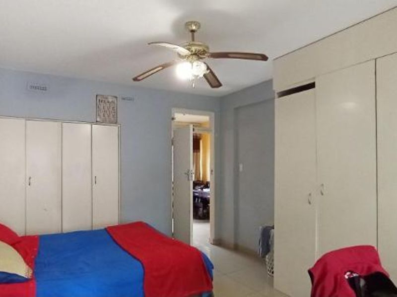 A bedroom featuring extensive built-in cupboard storage and a central ceiling fan, providing functional space with neutral finishes.