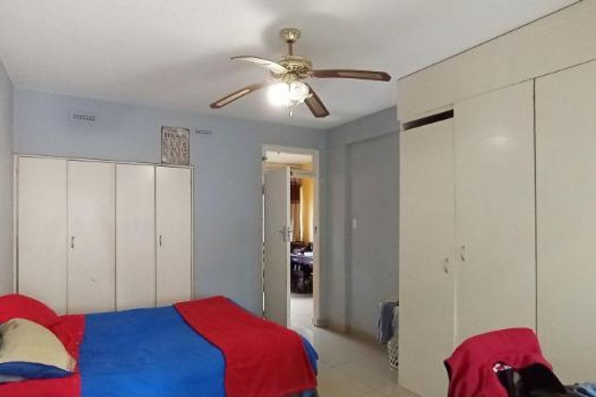 A bedroom featuring extensive built-in cupboard storage and a central ceiling fan, providing functional space with neutral finishes.