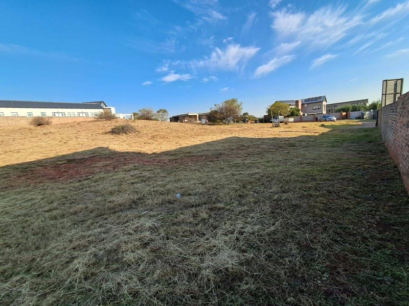 A vacant residential plot featuring dry grass and a perimeter brick wall, offering a clear space for future development.