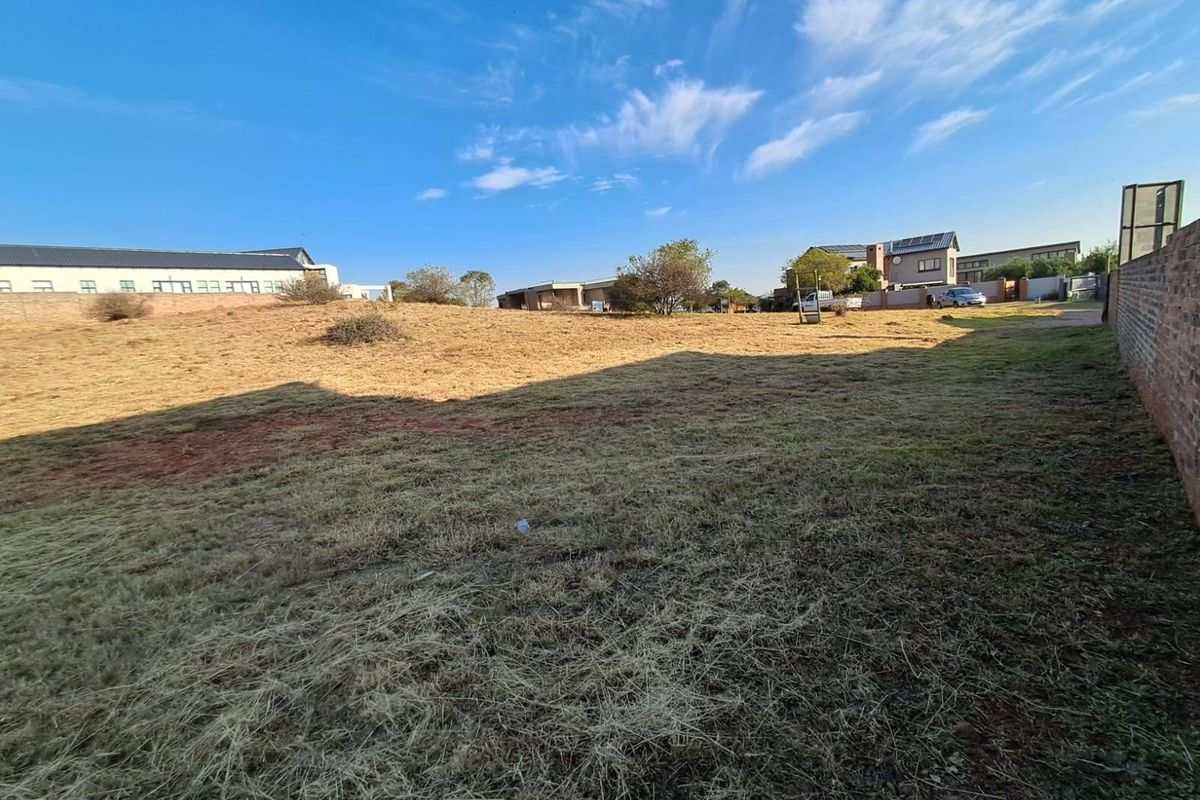 A vacant residential plot featuring dry grass and a perimeter brick wall, offering a clear space for future development.