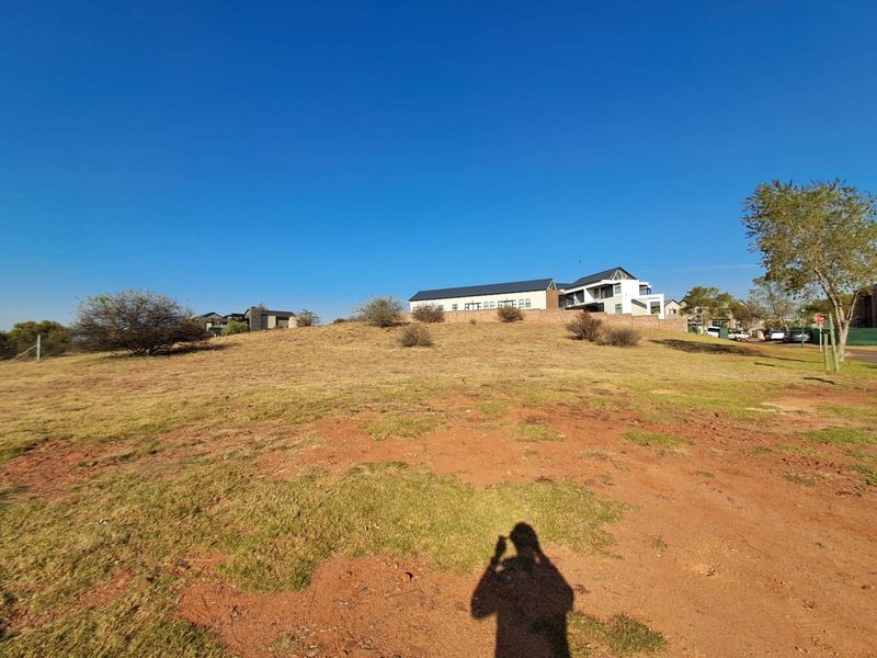 A wide-angle view of a vacant residential plot featuring natural grassland and surrounding neighborhood infrastructure.