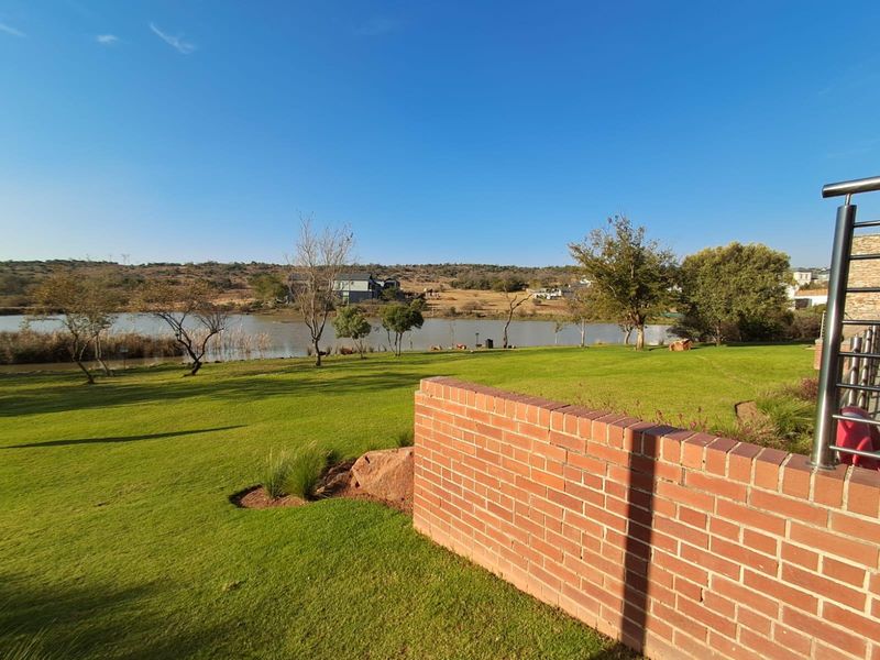 A scenic view of a well-maintained lawn leading to a tranquil waterfront, featuring a brick boundary wall in the foreground.
