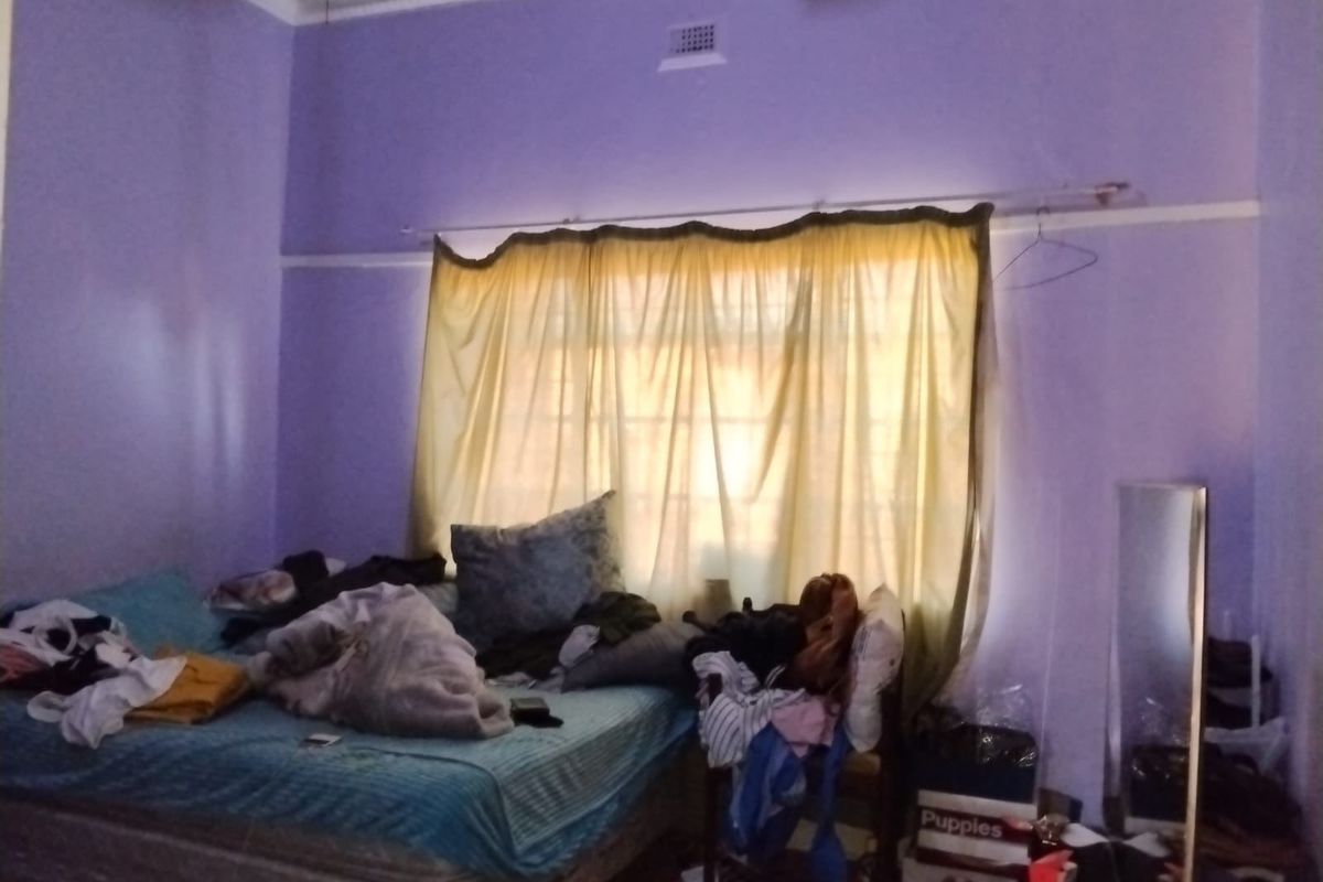 A bedroom featuring purple walls, a ceiling ventilation grille, and decorative cornice, requiring cosmetic updates to improve the overall aesthetic.
