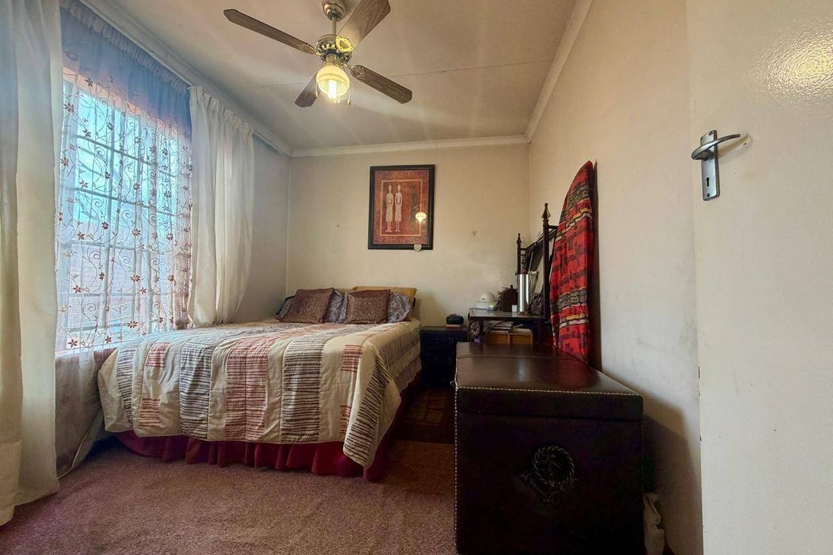 A bedroom featuring a ceiling fan and a window with security bars, requiring cosmetic updates to the flooring and wall finishes.