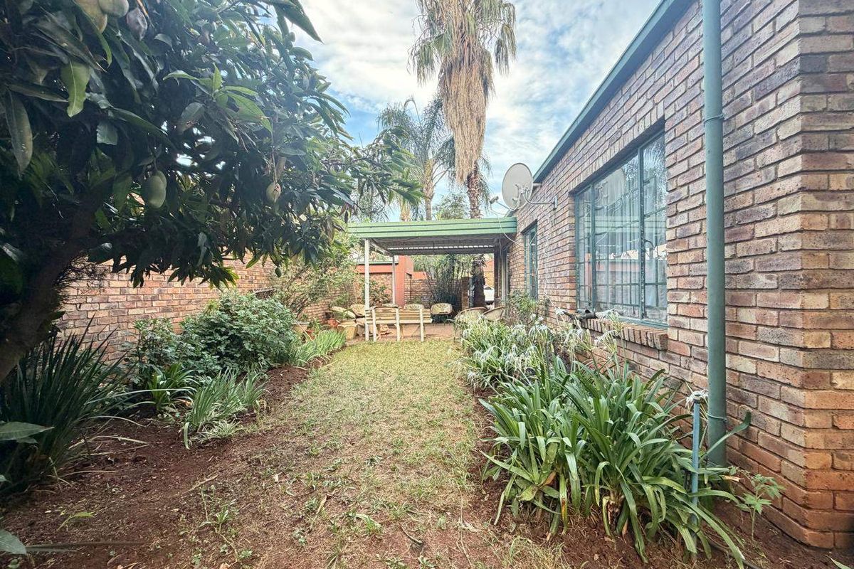 Rear exterior view of the townhouse featuring a brick facade, a covered patio area, and a private garden space with established landscaping.